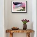 Riof Beach landscape print displayed in a black frame above a rustic wooden console table with purple tulips.