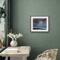 Light Ascending seascape giclée print displayed in a black frame with white mount against a muted green wall above a wooden desk.