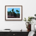 Reaching Stillness woodland giclée print displayed in a dark wooden frame with a white mount above a black sideboard with books and plants.