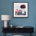 Traces of Home giclée print by Louise Turnbull displayed in a black frame with white mount above a dark console table against a blue wall.