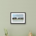 Silverburn Reflections landscape giclée print by Louise Turnbull displayed in a black frame with white mount above a light wooden cabinet against a sage-green wall.